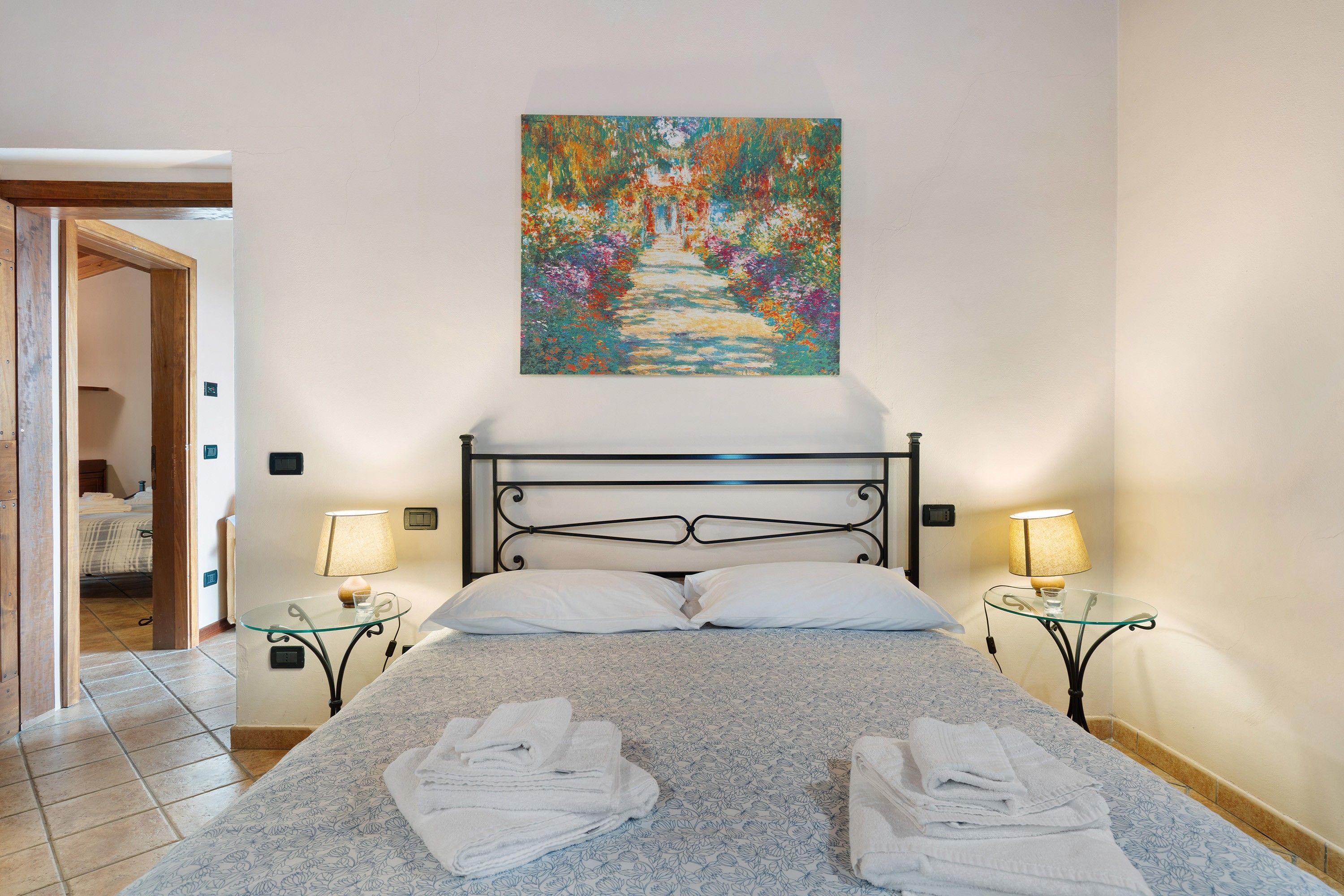 Une chambre d’hôtel avec un lit, deux tables de chevet, un tableau au mur et une porte donnant sur une autre pièce.