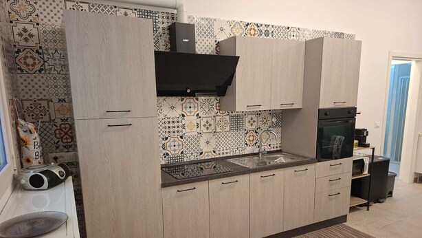 A modern kitchen with light wood cabinets, a black countertop, and patterned backsplash tiles. - New, detached vacation home near Taranto, ideal for 2-4 people. (Montemesola)