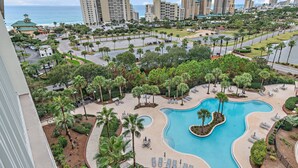 A resort with a large pool, palm trees, and a view of the ocean. - Luau II 6922/6924 - By the Sea (Miramar Beach)