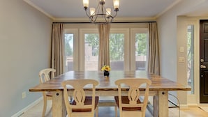 A dining room with a large wooden table, four chairs, a chandelier, and a vase with flowers. - The Landing at Wheat St.| 2Br in the heart of USC (Columbia)
