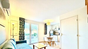 A compact living space with a sofa, a dining table with chairs, a kitchen area, and a sliding glass door leading to an outdoor area. - L’Échappée Belle, 4 guests, Pool in Calvisson (Calvisson)