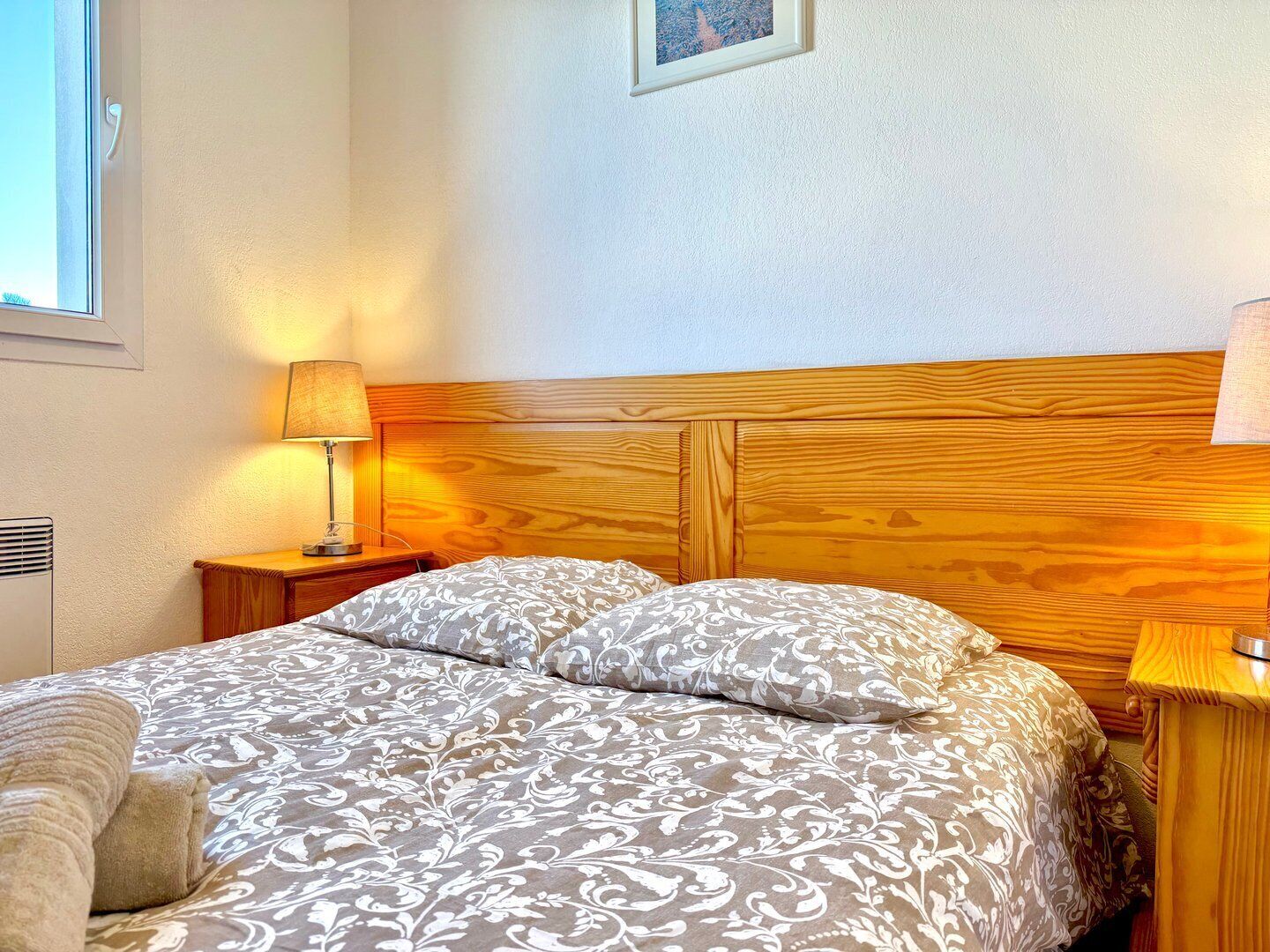 A neatly made bed with a patterned bedspread, a wooden headboard, and a bedside lamp on a nightstand.