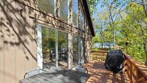 A wooden deck with a table and chairs, a barbecue grill, and a glass-enclosed patio area with a view of trees and a body of water. - Cece's Chalet: Hot Tub * New Owner Offer (Mount Jackson)