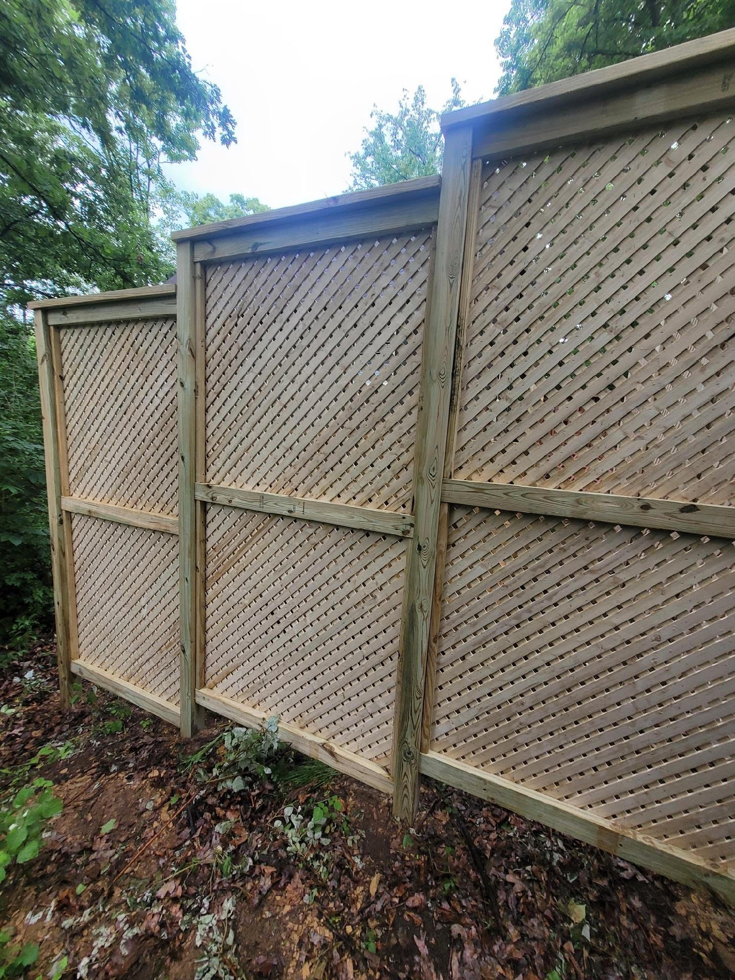 Une clôture en bois ornée d’un motif en treillis, probablement utilisée pour assurer l’intimité ou à des fins décoratives.
