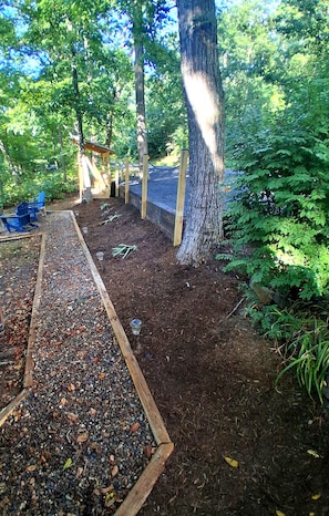 Ein Gartenbereich mit einem Holzweg, Bäumen und einer blauen Bank.
