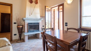 Un comedor con chimenea, mesa de madera, sillas y una planta en maceta.