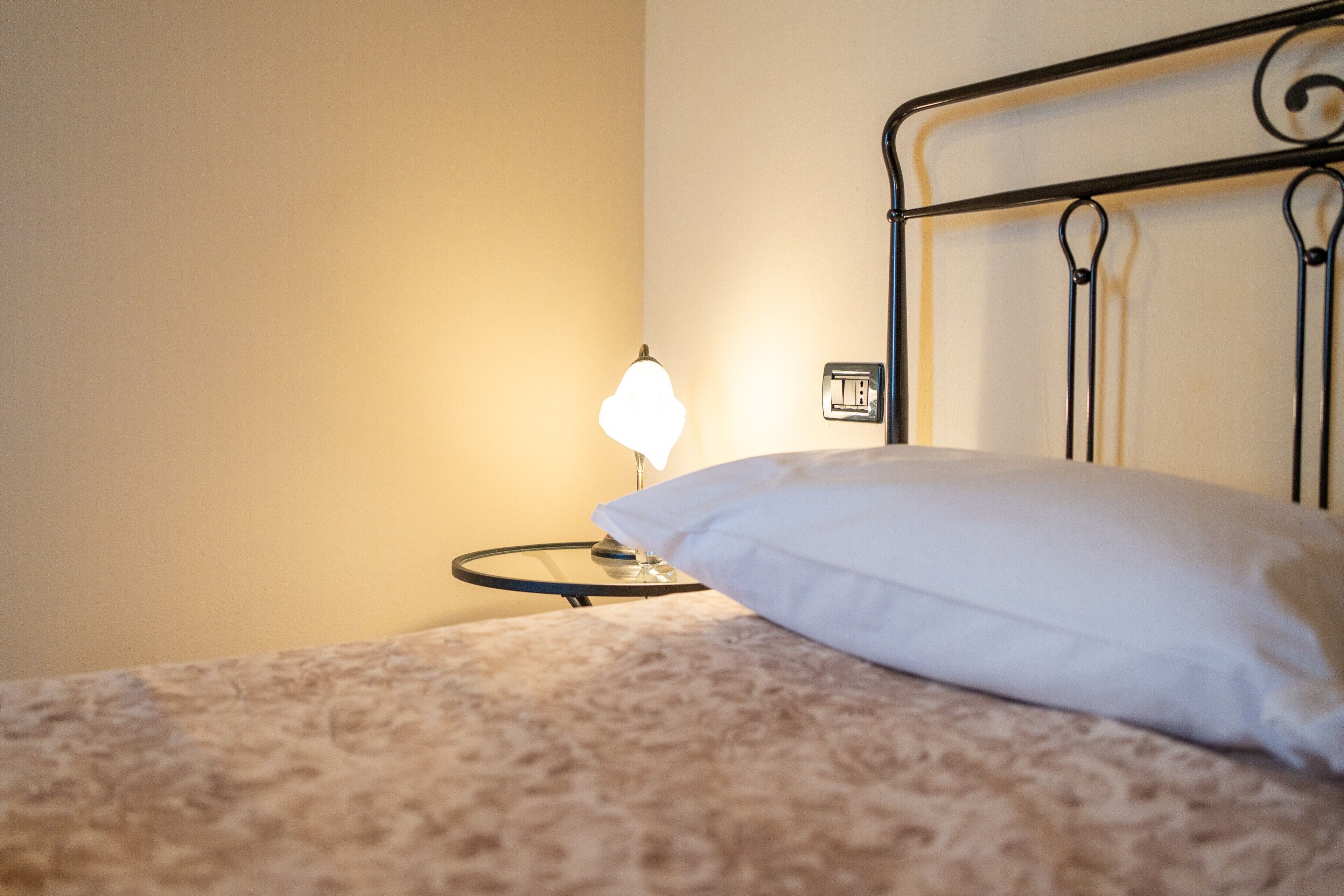 Un letto con un cuscino bianco, una lampada da comodino e una presa elettrica.