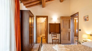 Un dormitorio con cama, un armario de madera, una silla y un baño visible a través de una puerta abierta.