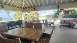 A covered outdoor seating area with wicker furniture, a ceiling fan, and a view of the ocean. - Harbor Haven Escape (Ruskin)