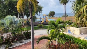 A view of a landscaped area with palm trees, a playground, and a beach in the background. - Harbor Haven Escape (Ruskin)