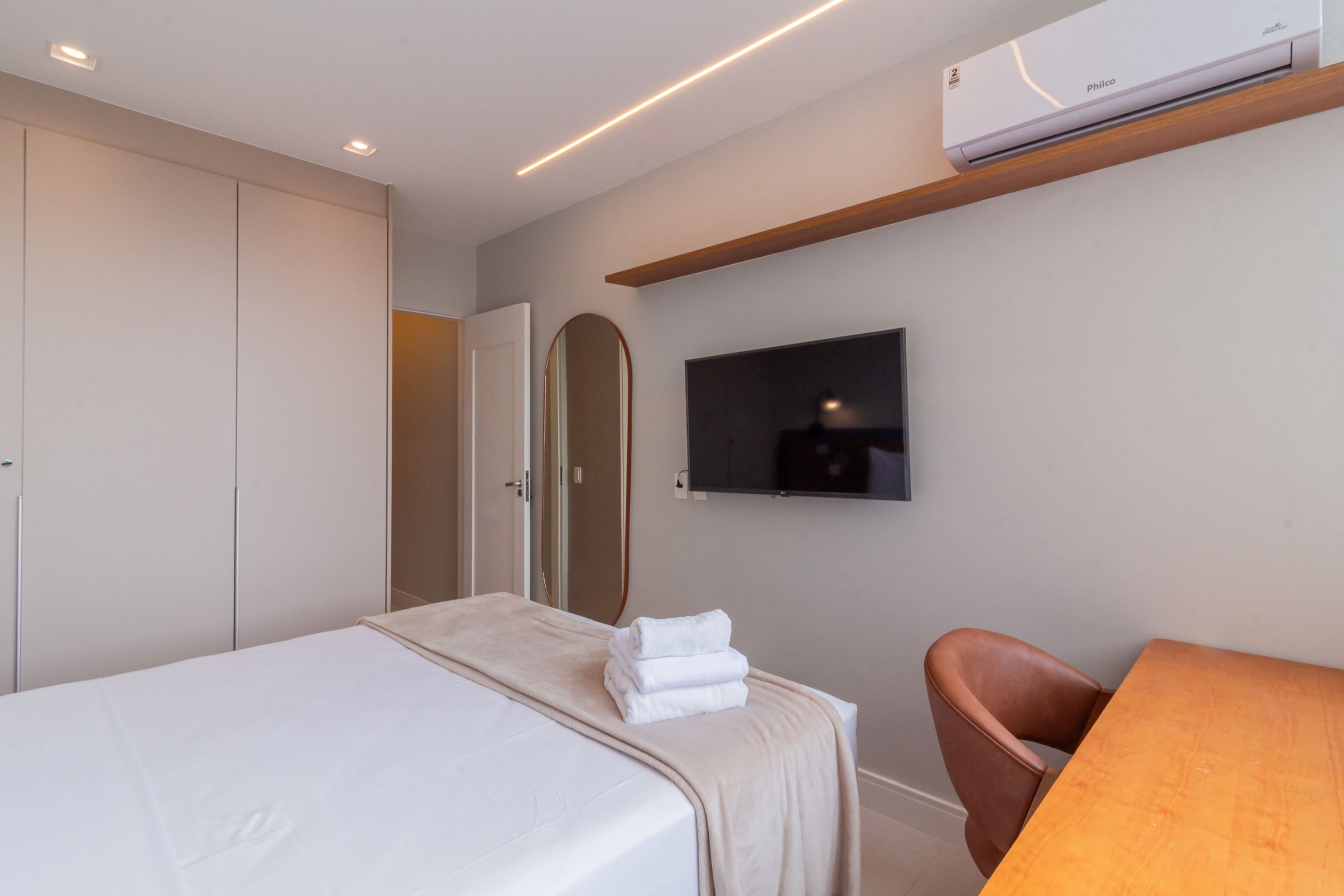 A hotel room with a bed, a TV mounted on the wall, a wooden shelf, and a chair.