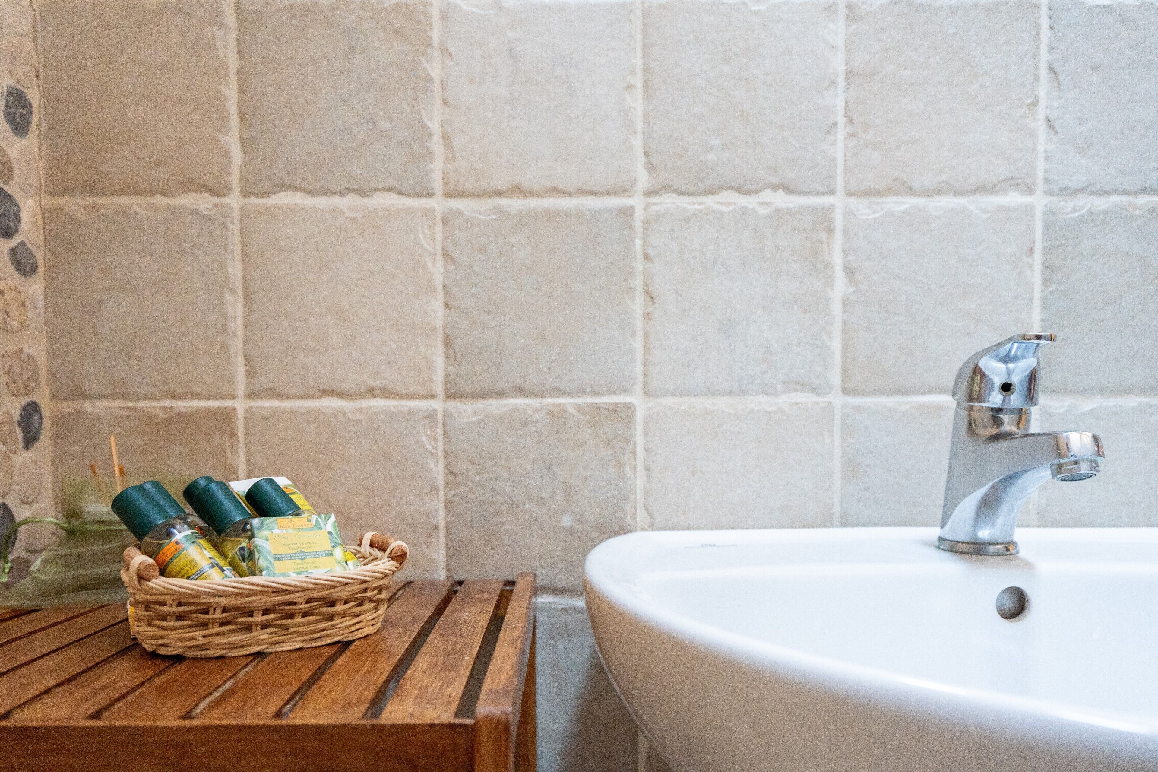 Une salle de bain avec un lavabo blanc, un robinet en métal et un banc en bois.