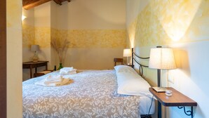 A hotel room with a bed, two bedside tables, a lamp, a vase with dried plants, and a wooden ceiling.