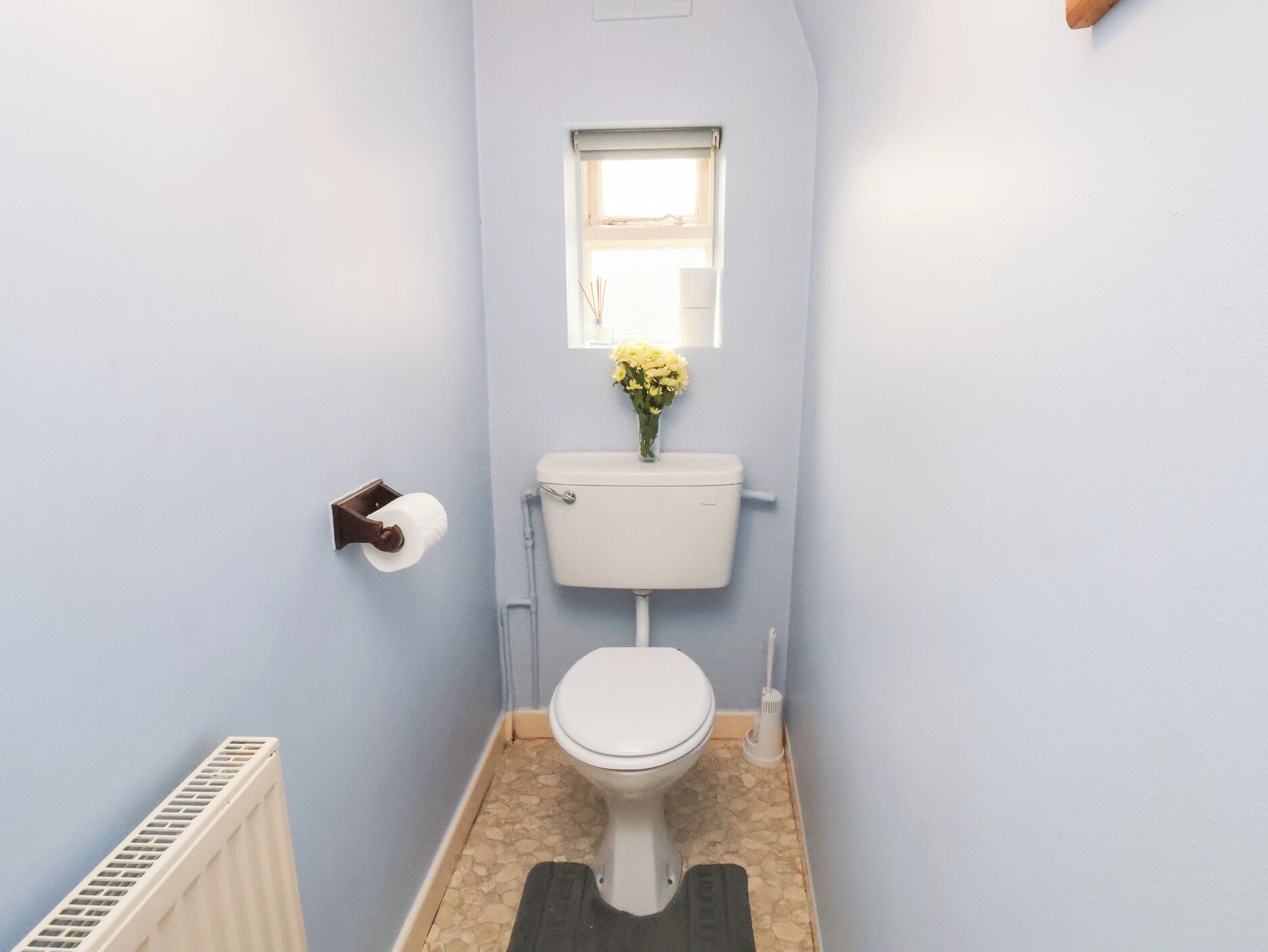 A small bathroom with a toilet, a window with flowers, and a radiator.