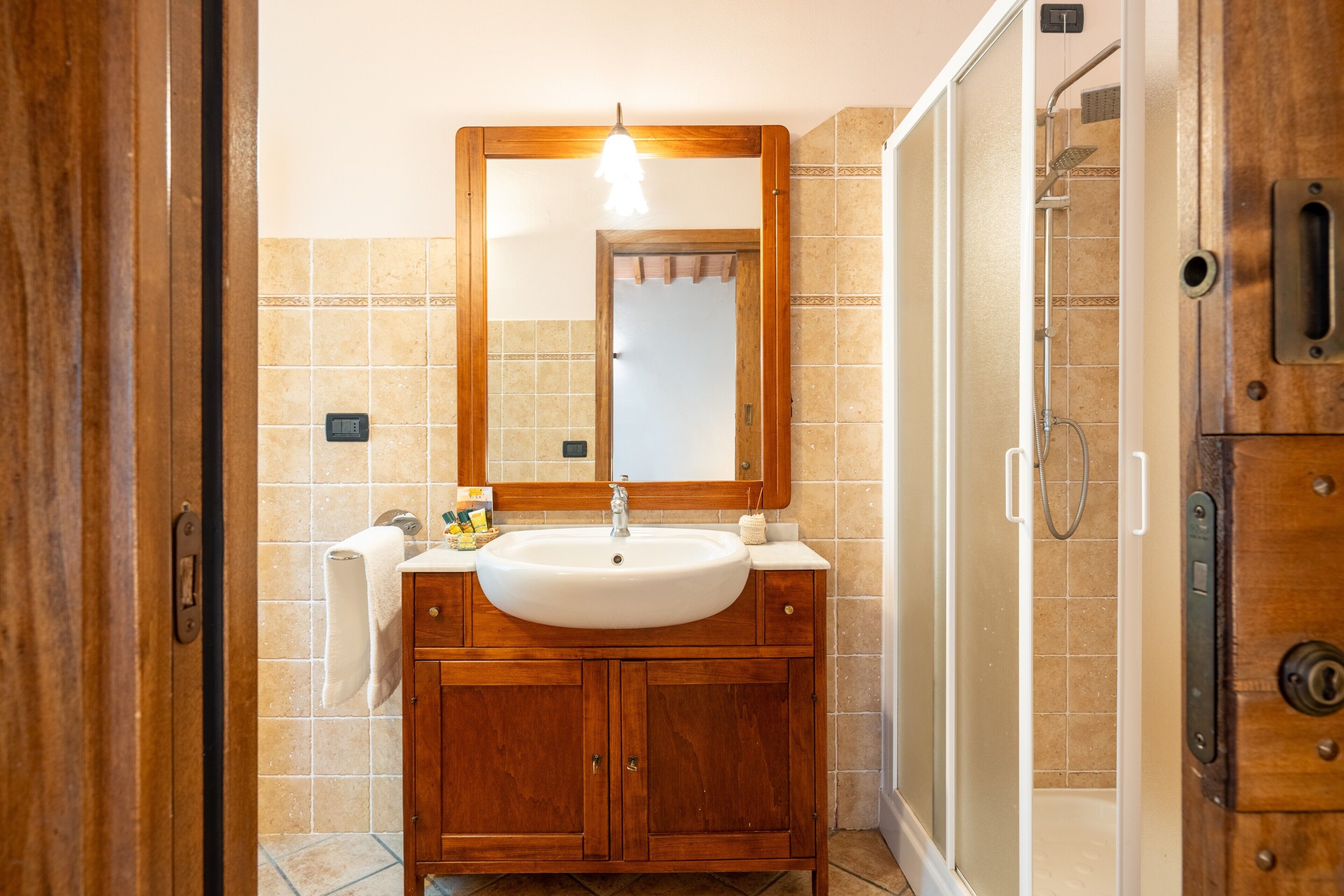 Un baño con tocador de madera, un lavabo blanco, un espejo y una zona de ducha.