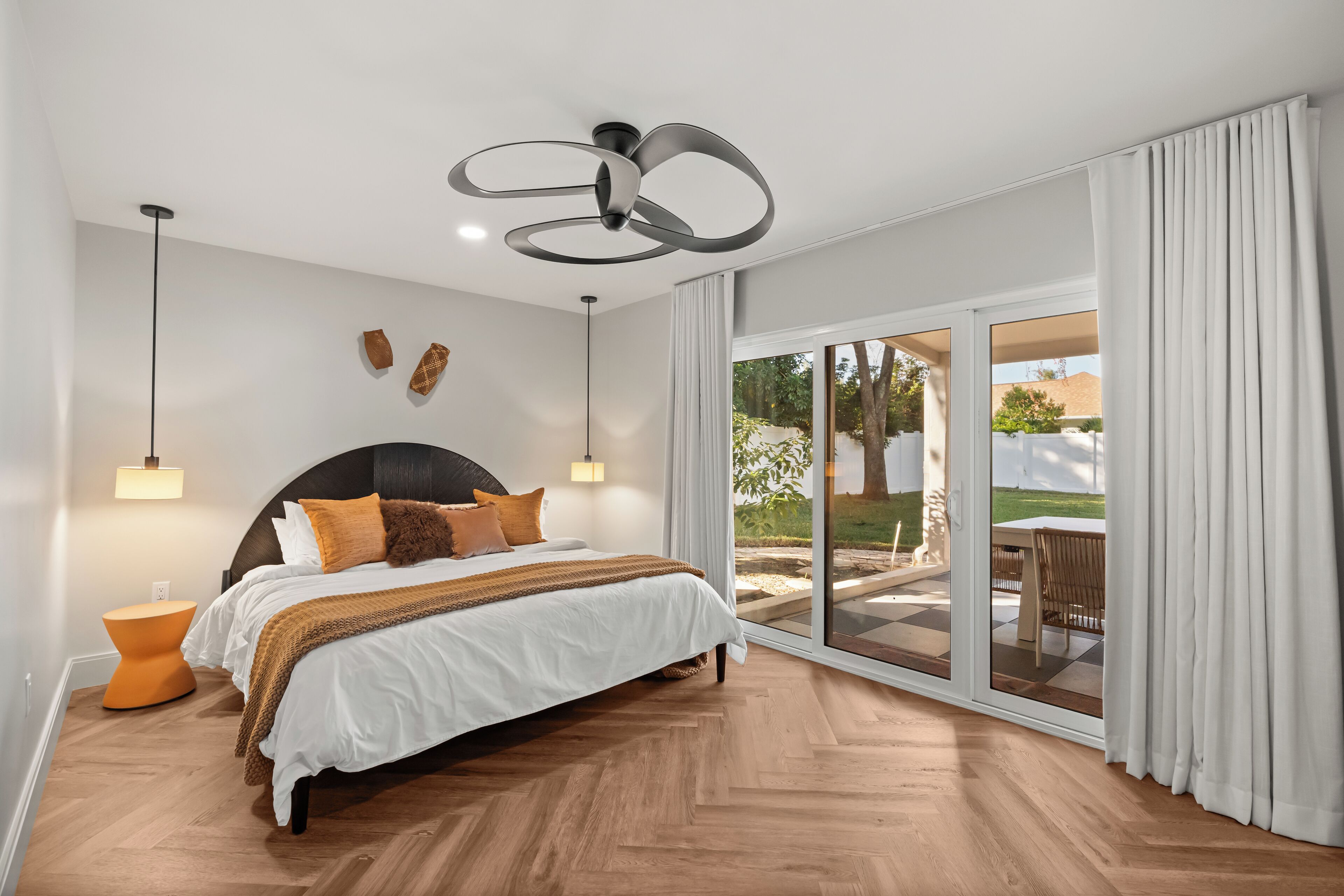 A bedroom with a large bed, a ceiling fan, a nightstand, and a view of the outdoors through a sliding glass door.