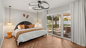 Une chambre dotée d’un grand lit, d’un ventilateur de plafond, d’une table de chevet et offrant une vue sur l’extérieur grâce à une porte-fenêtre coulissante.