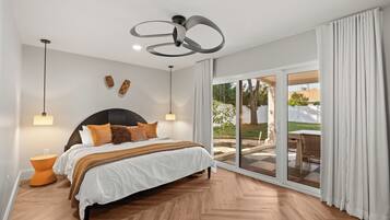 A bedroom with a large bed, a ceiling fan, a nightstand, and a view of the outdoors through a sliding glass door.