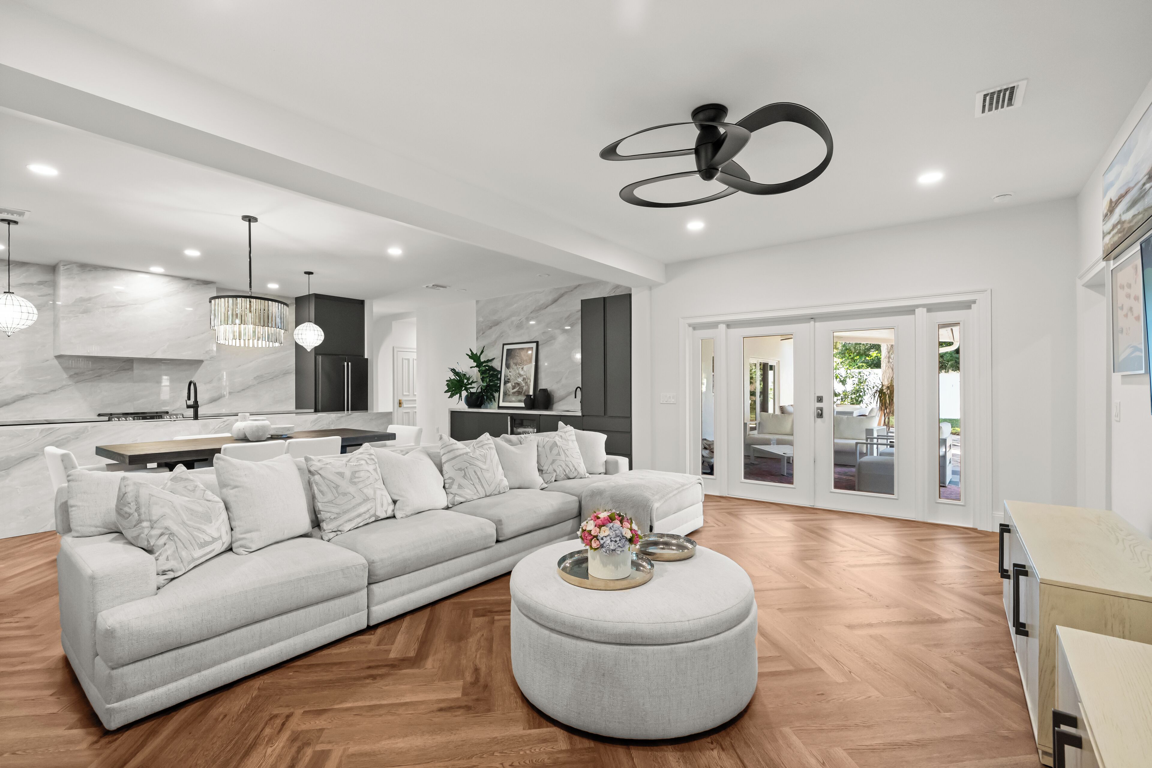 A modern living room with a grey sectional sofa, a round ottoman with a vase, and a dining area with a wooden table.