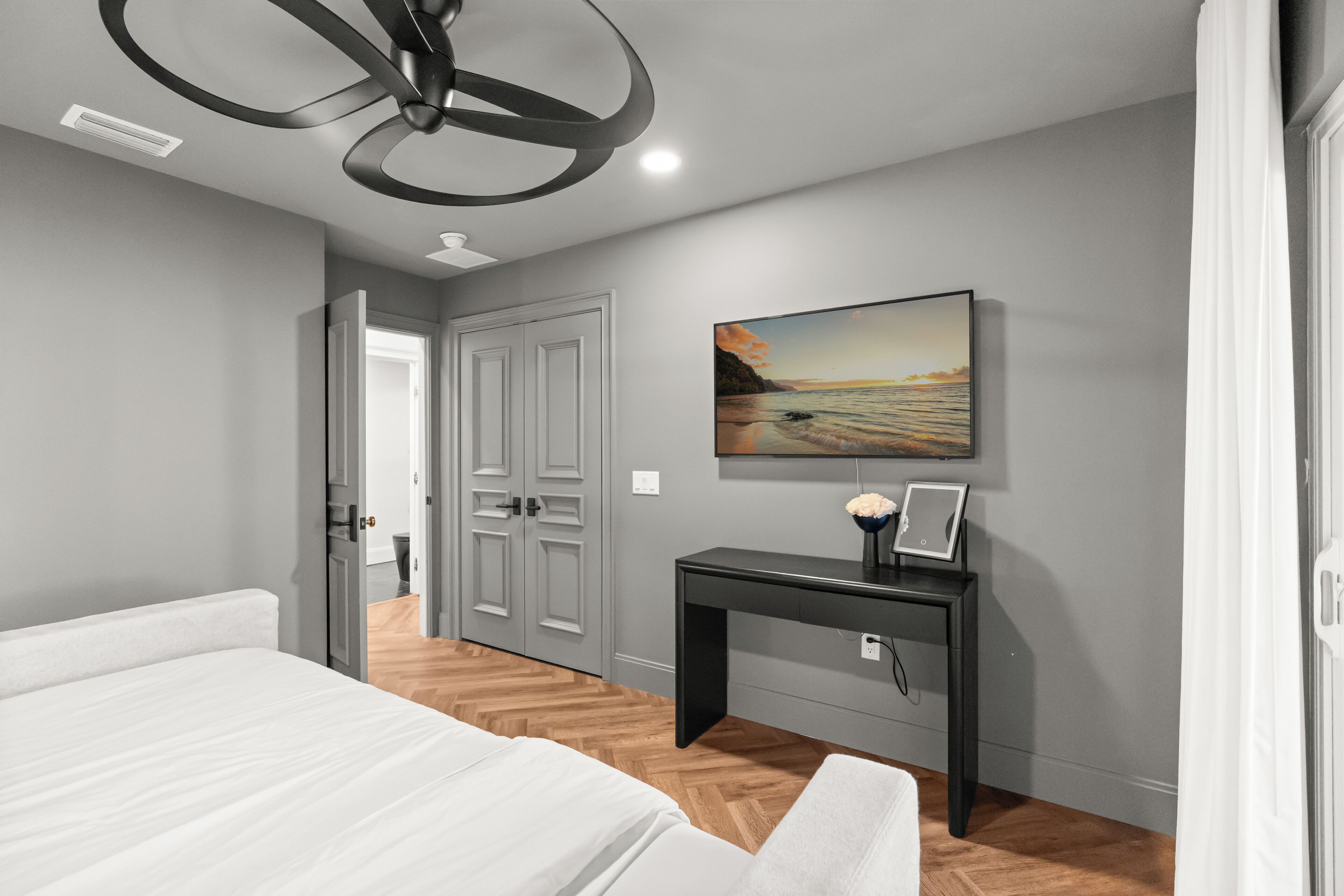 A bedroom with a bed, a desk, a painting, and a door.