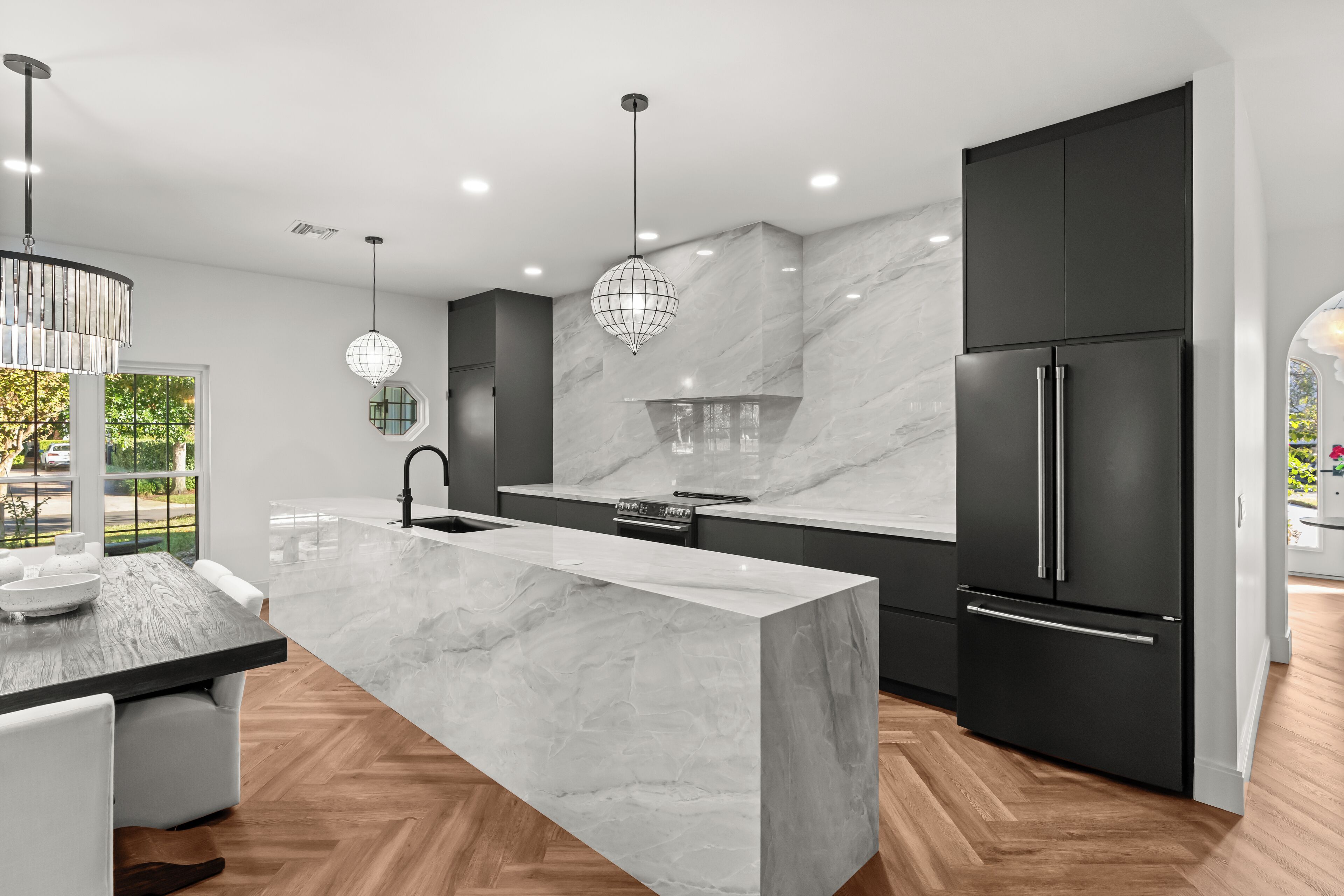 A modern kitchen with a marble island, dark cabinetry, stainless steel appliances, and pendant lighting.