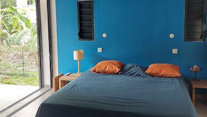 Quarto com uma cama grande, duas mesas de cabeceira, uma luminária e janela com vista para área verde.