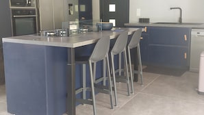Cozinha moderna com ilha central, banquetas, máquina de lavar louça e eletrodomésticos embutidos.