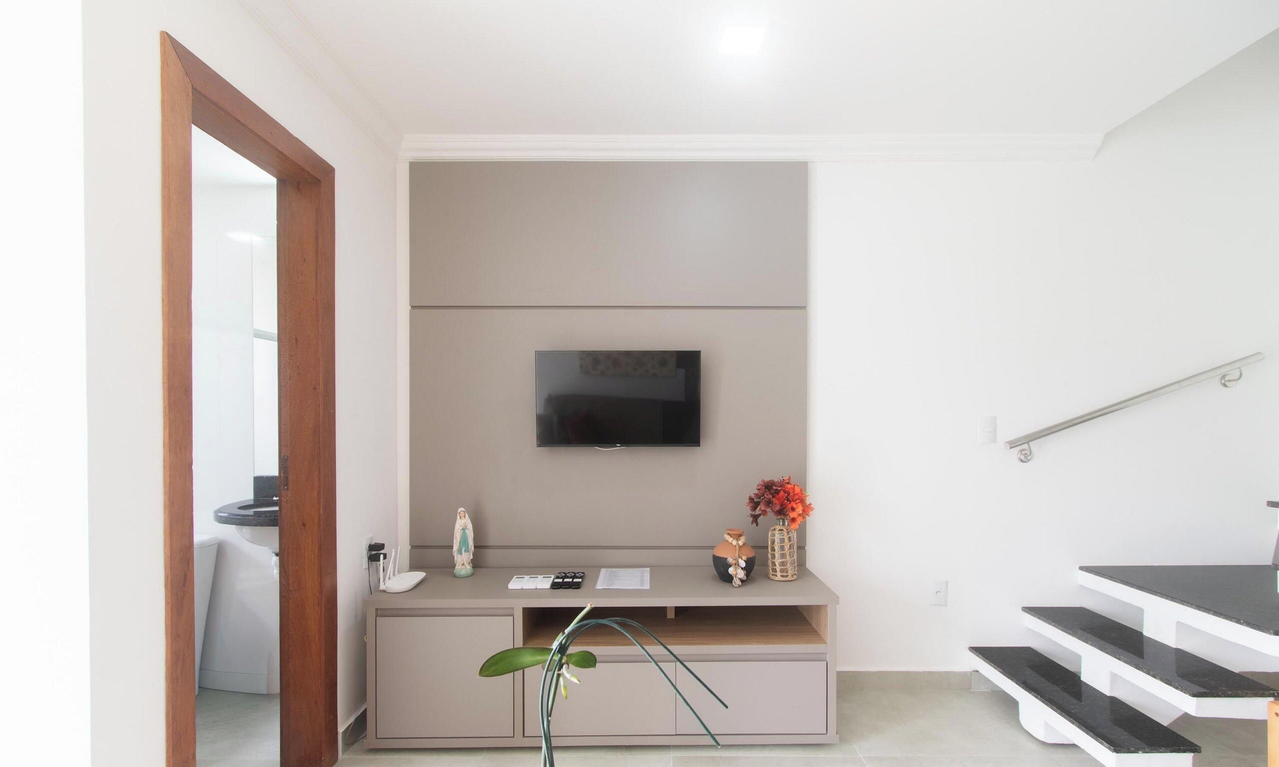 A modern living room with a flat-screen TV mounted on a wall, a small console table with decorative items, and a staircase leading to an upper level.