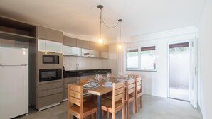 A modern kitchen with built-in appliances, a dining area with wooden chairs and a table set for four, and a sliding glass door leading to an outdoor area. - House 2 Suites in Condo w/ Pool Mnt0058 (Porto Seguro)