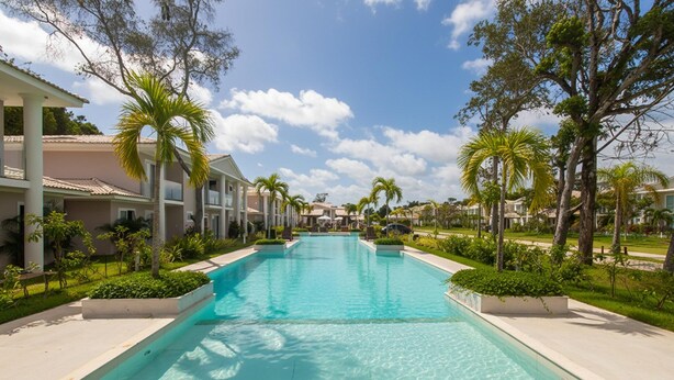 A swimming pool surrounded by palm trees and buildings with a clear blue sky. - House 2 Suites in Condo w/ Pool Mnt0058 (Porto Seguro)