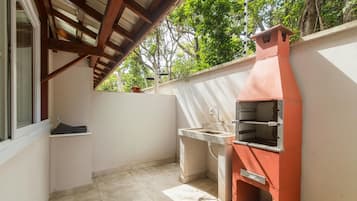A small outdoor kitchen area with a built-in oven and sink, under a wooden roof structure.