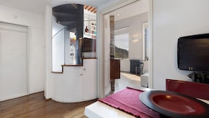 A modern interior with a curved staircase, a dining area with a red chair, and a view through an open door. - Villa 'Ancòra Tenuta Lonciano' with pool and view (Sesto Fiorentino)