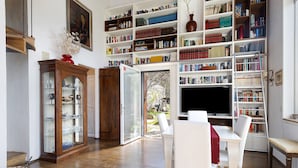 A room with a wooden floor, white furniture, a bookshelf, and a television. - Villa 'Ancòra Tenuta Lonciano' with pool and view (Sesto Fiorentino)