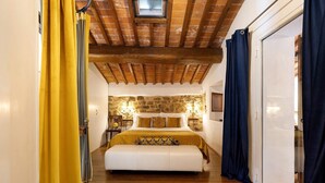 A bedroom with a stone wall, wooden beams, a bed with a bench, and a skylight. - Villa 'Ancòra Tenuta Lonciano' with pool and view (Sesto Fiorentino)