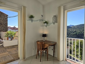 A corner room with a wooden table and chairs, a lamp, and a view of a mountainous landscape. - Le Nid de Paulilles in Port-Vendres (Port-Vendres)