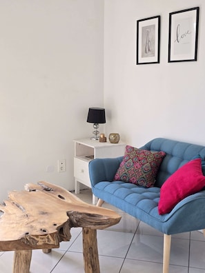 A modern living room with a blue sofa, a wooden coffee table, a white side table with a lamp, and two framed pictures on the wall. - Le Nid de Paulilles in Port-Vendres (Port-Vendres)
