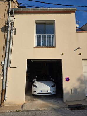 A white car parked in a garage attached to a beige building with a window and a no parking sign. - Le Nid de Paulilles in Port-Vendres (Port-Vendres)