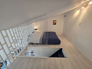 A modern bedroom with a sloped ceiling, a bed with patterned bedding, a small window, and a wall-mounted light fixture. - Le Nid de Paulilles in Port-Vendres (Port-Vendres)