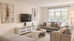 Ein Wohnzimmer mit einer Couch, einem Hocker, einem Couchtisch, einem Fernseher und Kunstwerken an der Wand.