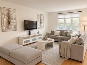 Ein Wohnzimmer mit einer Couch, einem Hocker, einem Couchtisch, einem Fernseher und Kunstwerken an der Wand.