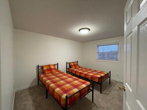 Ein Zimmer mit zwei Betten, einem Fenster mit Jalousien, einer Tür und einer Deckenleuchte.
