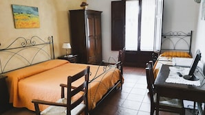 Une chambre à coucher avec un lit, un bureau avec un ordinateur, une chaise, une armoire et une fenêtre.