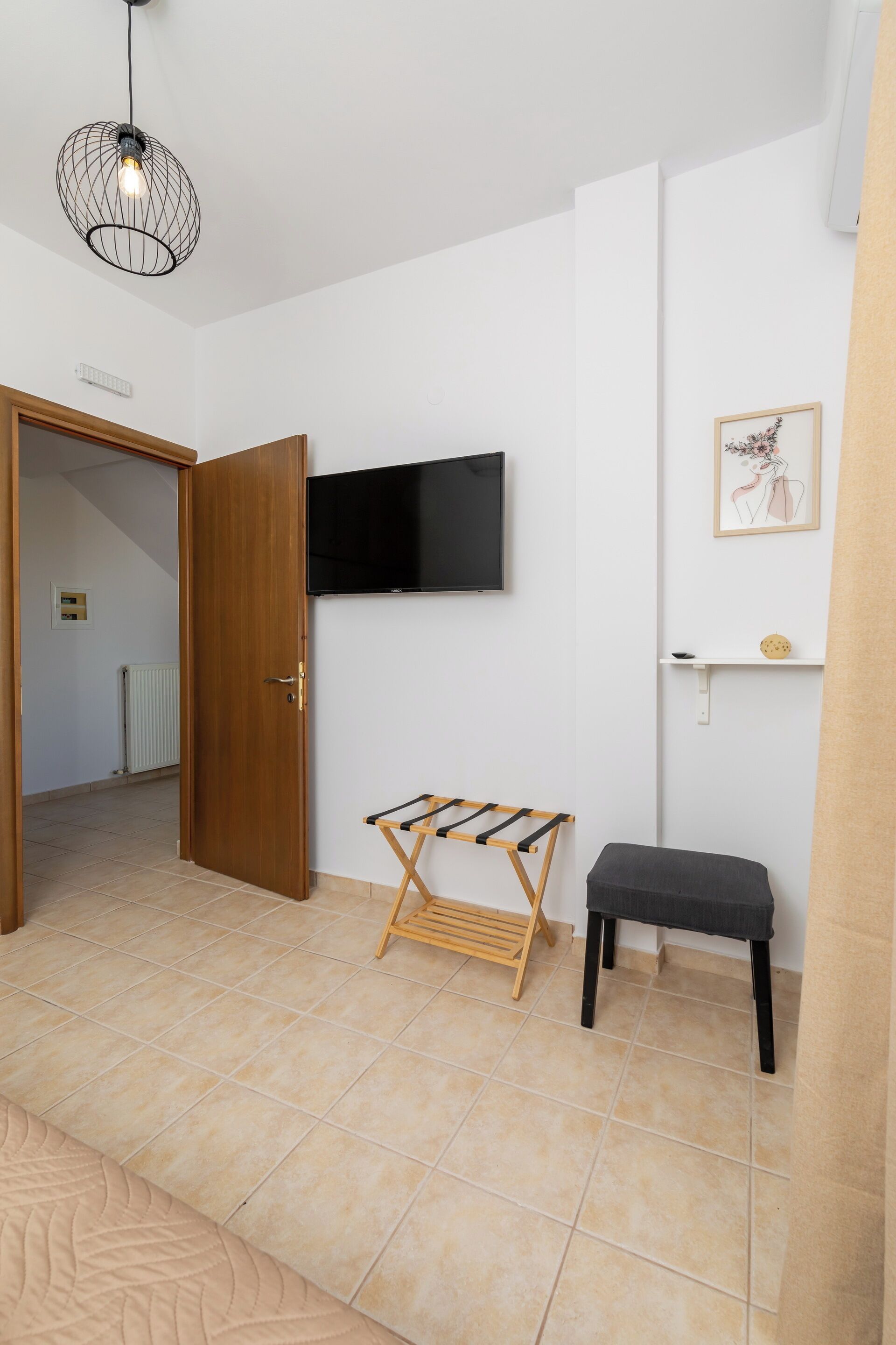 A room with a wooden door, a mounted TV, a drying rack, and a bench.