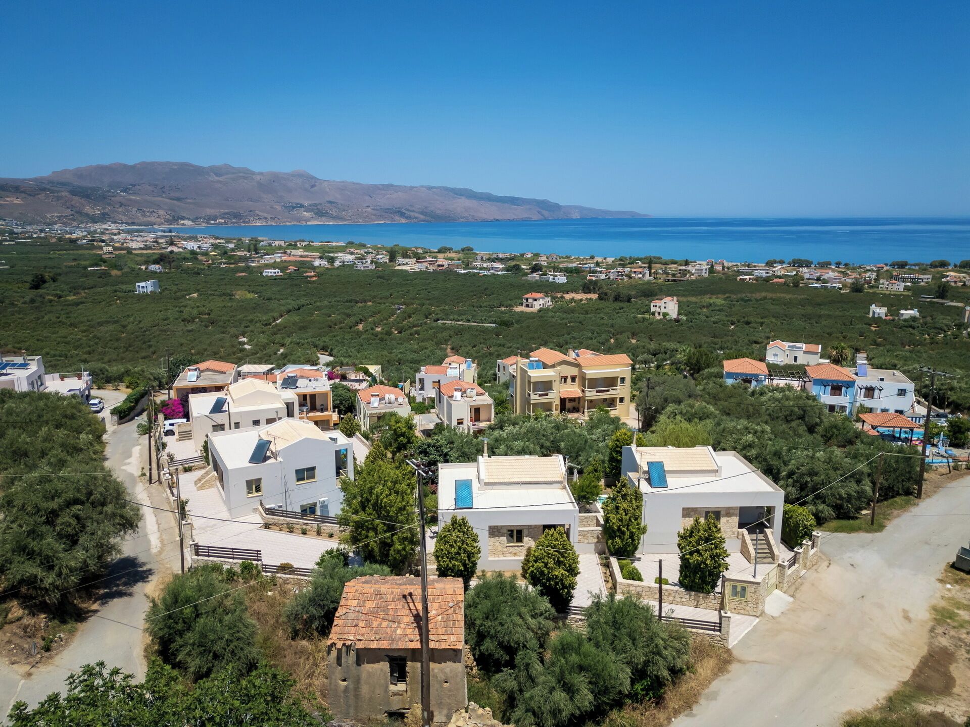 Zona residencial a la costa amb cases modernes, una vista clara del mar i un paisatge amb turons al fons.