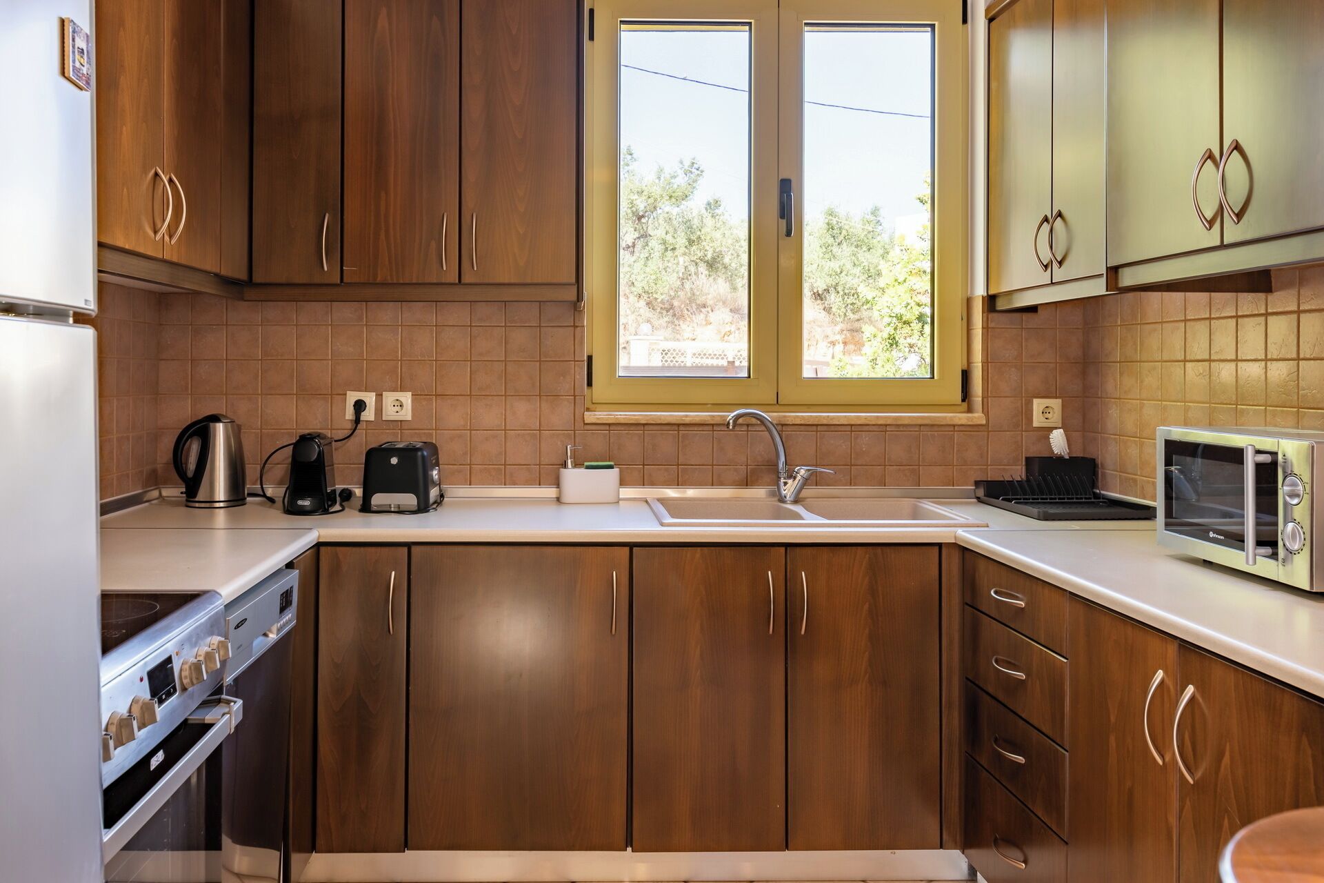 A kitchen with wooden cabinets, a built-in oven, a microwave, a kettle, a toaster, and a sink.