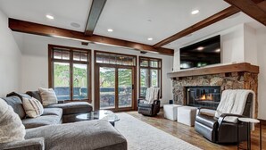A spacious living room with a fireplace, large windows, and a stone accent wall. - Platinum 3BR Beaver Creek Condo | Ski-in/Ski-out (Avon)