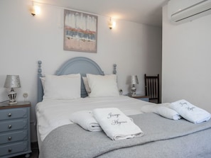 A neatly made bed with white and grey linens, two bedside lamps, a painting on the wall, and a folded towel with a name on it. - Dappan Bleu Apartment, Burgau, Algarve (Burgau)