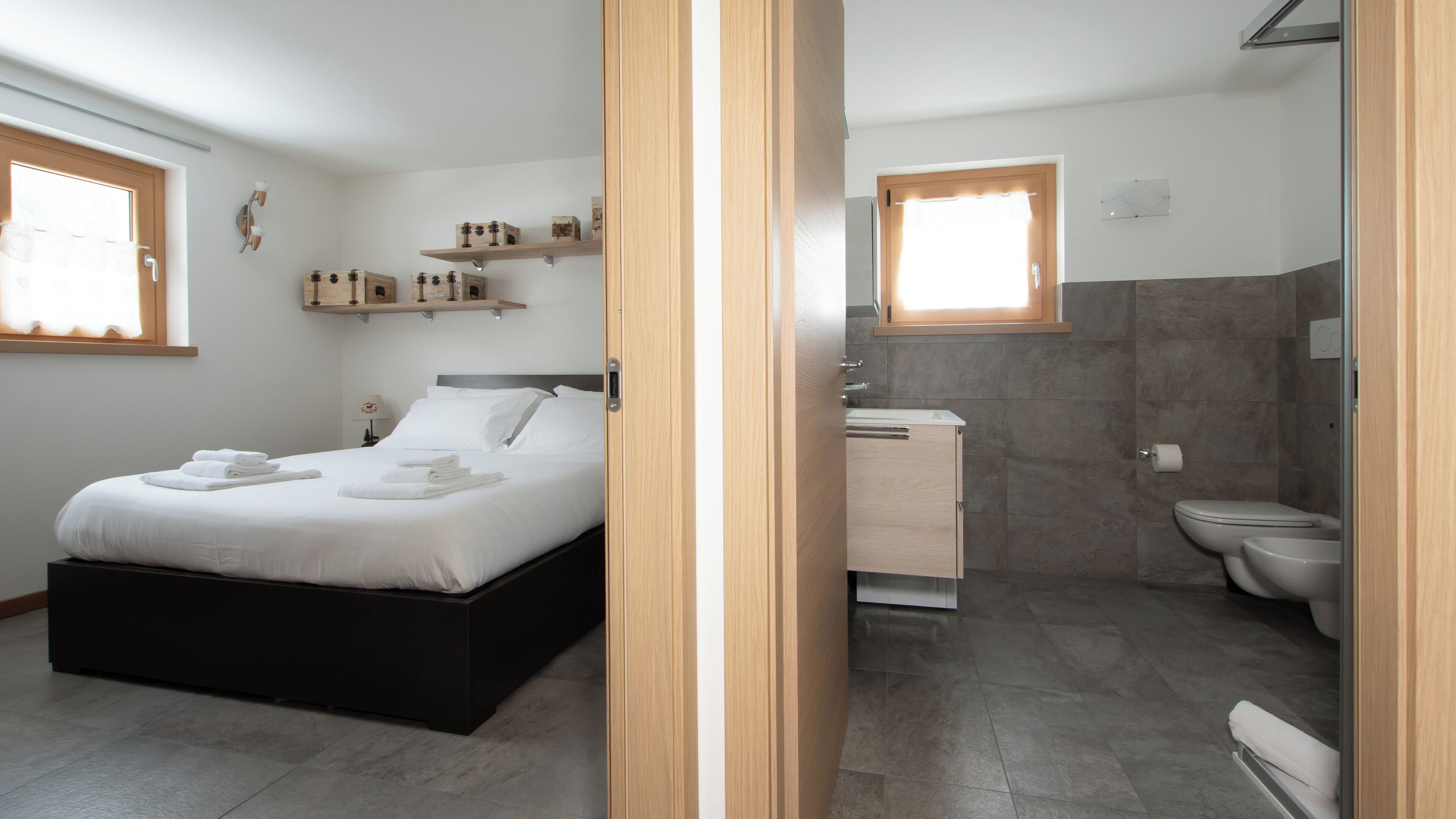 Een moderne slaapkamer met een bed, nachtkastjes en een badkamer met toilet en wastafel.
