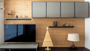 A modern living room with a flat-screen TV, wooden wall paneling, a small wooden Christmas tree, and a lamp. - Zardin 7 - One Bedroom Apartment, Sleeps 4 (Valdidentro)