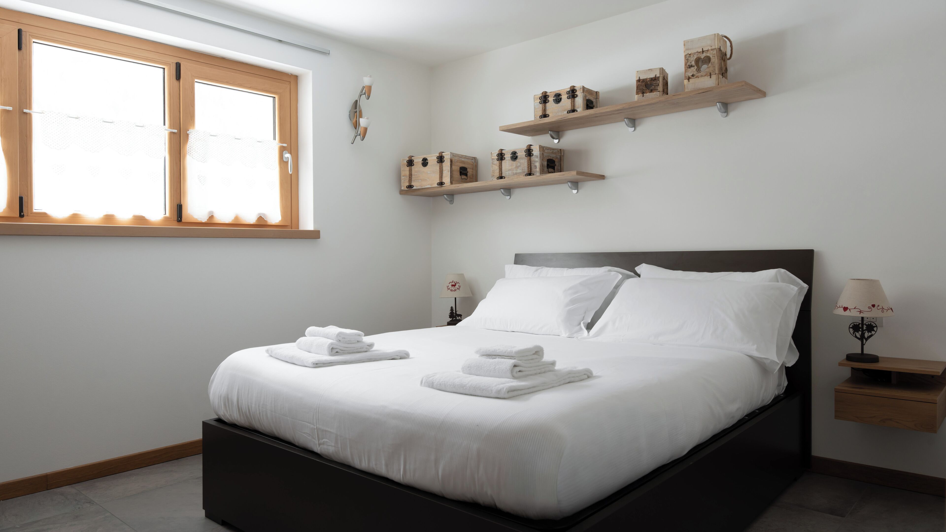 Un lit bien fait, avec du linge de lit blanc, une table de chevet avec une lampe et des étagères en bois au-dessus du lit.